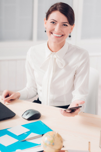 Professional woman smiling at desk with smartphone and laptop in office.