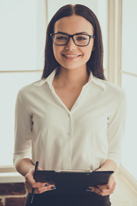Professional woman in white blouse and glasses holding a clipboard, smiling in an office environment