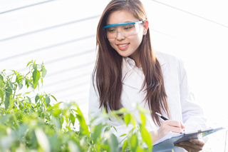 Female agricultural scientist with safety glasses taking notes in a greenhouse.