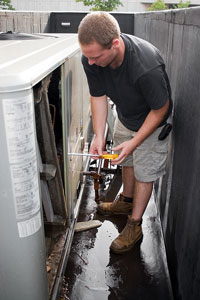 Man repairing outdoor air conditioning unit in a narrow space