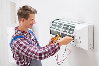 Technician repairing air conditioner unit with multimeter in hand