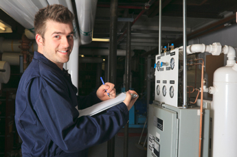 HVAC technician with clipboard inspecting industrial heating system in a mechanical room.