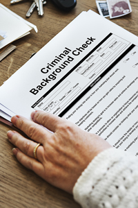 Person reviewing a criminal background check form on a desk surrounded by various objects including pens and papers.