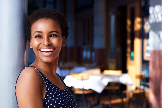 Young woman smiling outdoors by a cafe in a polka dot dress.