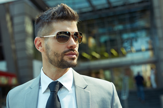 Stylish young man in sunglasses and suit standing in an urban setting