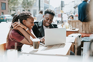 Young couple enjoying coffee and laptop at an outdoor cafe table.