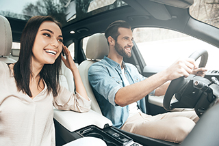 Man driving a car and Woman passenger enjoying the ride, both wearing seat belts in a modern vehicle interior during daylight.