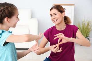 Young girl and woman in purple shirt playing hand game in living room with couch in background.