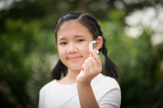 Young girl holding a hearing aid in focus with a blurry green background