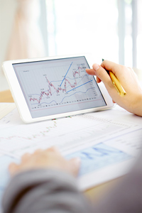 Person analyzing financial charts on a tablet with a stylus pen in a bright office setting.