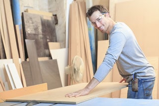 Smiling carpenter working in a workshop handling large wooden board