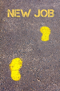 Yellow footprints and text "NEW JOB" painted on asphalt road, symbolizing career change or job search direction.
