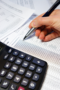 Close-up of a hand using a pen to work on financial documents with a calculator nearby