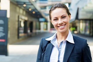 Professional young woman in business attire smiling confidently outdoors.