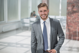 Smiling young businessman in gray suit standing in an office environment