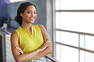Confident professional woman in yellow blouse smiling with arms crossed in an office setting