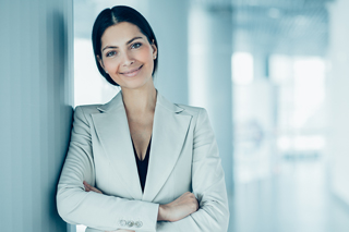 Professional woman in light gray suit standing confidently in an office environment.