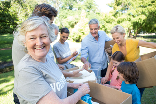 Group of diverse volunteers of various ages packing donations in cardboard boxes at a sunny park