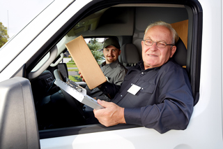 Two smiling delivery men in a van, one holding a clipboard and package, ready to make a delivery.