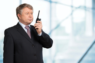 Mature businessman in suit using walkie-talkie in an office building.