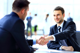 Two businessmen shaking hands across a table in a bright office setting