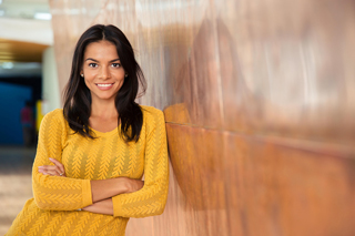 Woman in yellow sweater smiling confidently while leaning against a wooden wall indoors