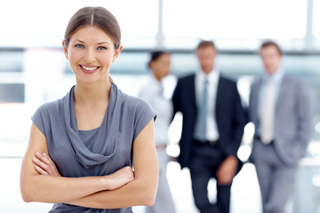 Confident businesswoman with crossed arms smiling, with male colleagues in background in office setting.