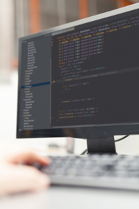 Close-up view of a computer screen displaying code with a person's hands typing on a keyboard in the foreground.