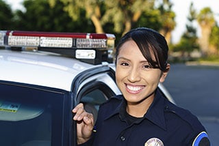Two smiling police officers standing beside a patrol car in daylight.
