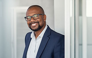 Businessman with glasses wearing a blue suit and white shirt standing in an office environment.