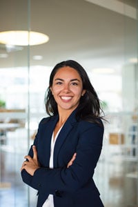 A smiling woman dressed in a blue blazer and white shirt standing with her arms folded across her chest