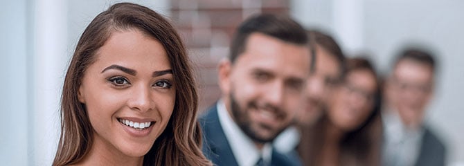 A smiling young professional woman sitting near a group of people in business attire