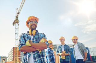 Construction worker in orange hard hat and reflective vest - colleagues discuss in the background near a crane on a sunny day.