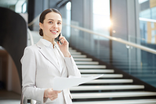Businesswoman in white suit talking on smartphone and holding documents in office building.