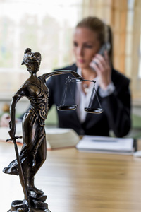 Woman lawyer on phone with focused statue of Lady Justice in foreground