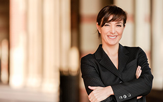 Professional woman in black suit smiling confidently with arms crossed in a corporate environment with columns in the background