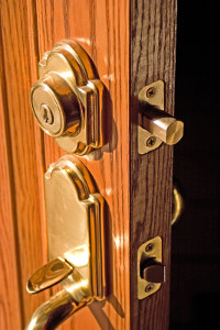 Close-up view of a shiny brass door handle and lock on a wooden door with latch and hinges visible.