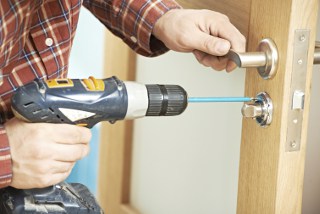 Person installing a door knob with a power drill, focusing on door hardware installation.