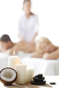 A relaxing spa setting with a couple receiving massages, featuring candles, coconut, and massage stones.