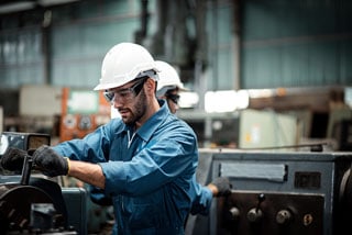 Industrial worker in blue uniform and white helmet operating machinery in a factory setting