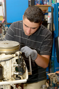 Young mechanic repairing a small engine at an automotive shop, wearing gloves and focusing intently on his work.