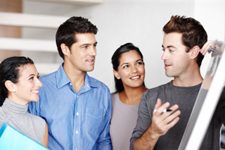 Group of four young professionals discussing over a laptop in an office setting.
