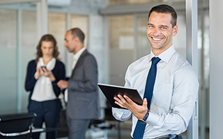 Businessman holding a tablet in office with colleagues discussing in the background.