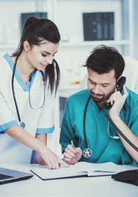 Two healthcare professionals working at a desk in a clinic - one on the phone and the other taking notes.