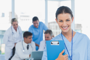 Nurse holding clipboard in hospital with colleagues discussing in background