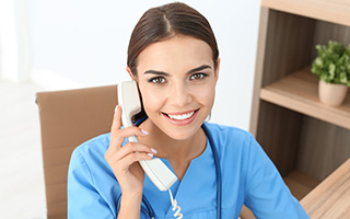 Dental office receptionist in blue scrubs speaking on telephone in office setting