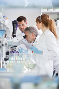 Medical laboratory technicians analyzing samples, with one using a microscope in a modern lab setting.