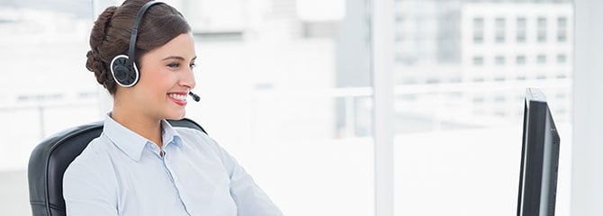 Female medical transcriptionist smiling and wearing a headset while at a computer in a well-lit office with large windows