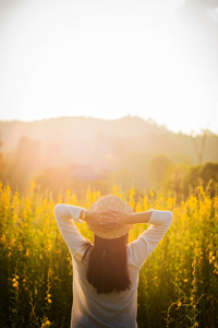 Woman in straw hat enjoying sunset in a field of yellow flowers