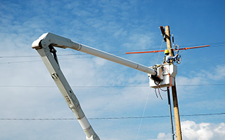 Utility worker in a bucket lift repairing electricity lines on a power pole against a blue sky with clouds
